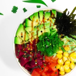 Imagen de un delicioso Poké Bowl vegano con ingredientes coloridos y frescos en un tazón de cerámica sobre un fondo blanco.